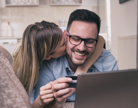 Young couple lying on sofa, looking at laptop and holding credit card. Online shopping conceptの写真素材