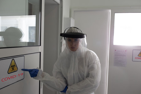 Woman in protective suit and safety mask showing covid sign in laboratory