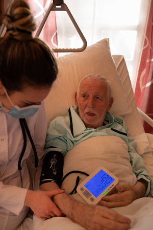 Young nurse measuring blood pressure to senior man lying in bed in hospitalの写真素材