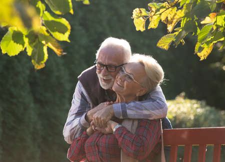Senior man and woman hugging in garden on autumn sun