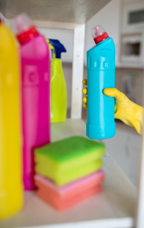 Close up of female hand with protective gloves taking bottle with cleaning products from shelf