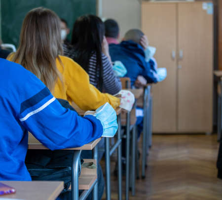 Close up of pupil's hand with safety mask on school desk in classroom during lesson. Pandemic protection conceptの写真素材