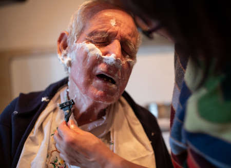 Wife helping senior man to shave beard at homeの写真素材