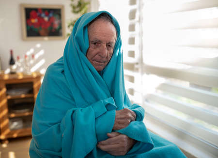 Senior man covered with blanket over head sitting in wheelchair beside window at homeの写真素材