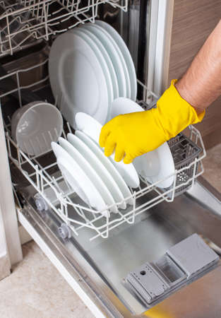Close up of male hands with gloves loading dishwasher with white platesの写真素材
