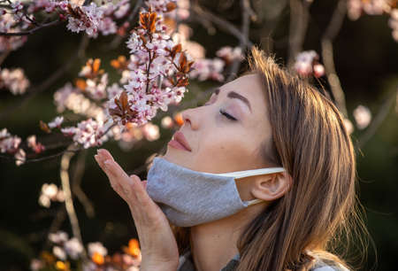 Pretty young girl with facial mask smelling blooming tree. Spring allergy protection conceptの写真素材