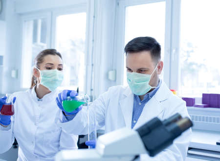 Young scientists researching experimenting holding erlenmeyer flask. Man and woman lab technician in...