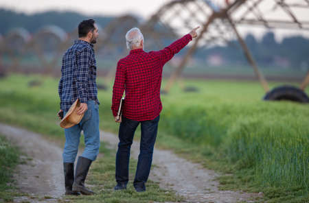 Two men walking next to field looking pointing showing center pivot irrigation system. Farmers...