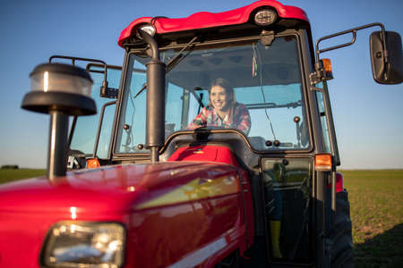 Female farmer sitting in agricultural machinery. Woman driving red tractor looking forawrd smiling.の写真素材