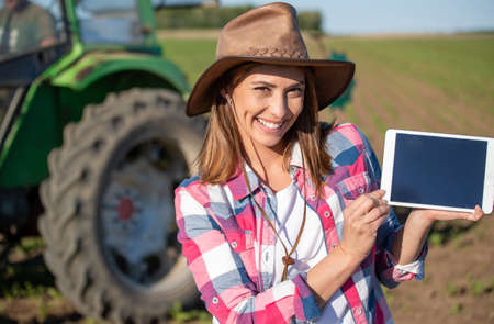 Young woman using modern technology in agriculture looking at camera. Farmer standing in field in...