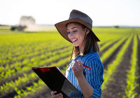 Portrait of female agronomist taking notes on growth of corn. Young farmer standing in field smiling satisfied.の写真素材