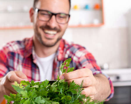 Husband cutting herbs parsley preparing food.. Young man blurry standing in background smiling.の写真素材