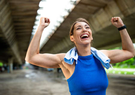 Young woman happy because of success win after exercising. Athlete wiping sweat with towel on neck after victory running.の写真素材