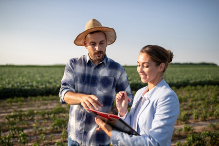 Male farmer wearing plaid shirt and straw hat pointing explaining. Young female insurance sales...