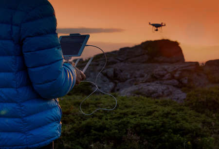Close up of male's hands holding remote control and driving drone above rocks on mountain peak