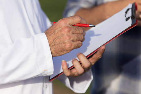 Close up of senior man hands holding notebook and writing notes in fieldの写真素材