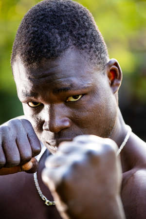 Muscular African boxer holding fists in chin height for defence and preparing to kickの写真素材