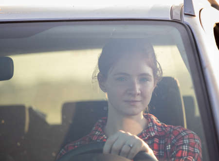 Attractive ginger girl sitting in car looking ahead. Young redhead driving car looking at camera.の写真素材