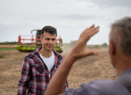 Two farmers standing in soy field and talking while combine harvester working in backgroundの写真素材