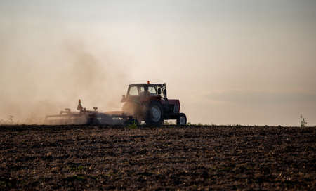 Tractor plowing field at sunset in late summer timeの写真素材