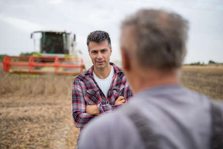 Two farmers standing in soyfield during harvest and talking. Younger man smiling and holding arms crossedの写真素材