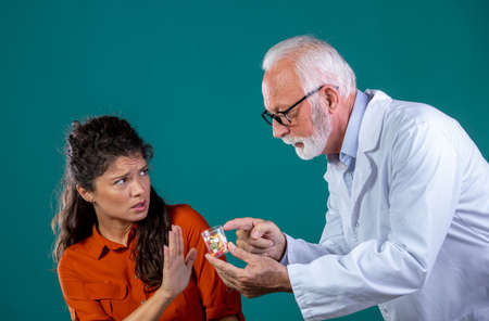 Senior experienced male doctor recommending bottle full of drugs to young woman patient that rejecting pills and showing stop sign with hand. Health care conceptの写真素材