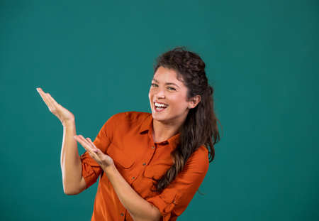 Pretty happy woman showing with hands on empty space beside her, on blue background in studioの写真素材