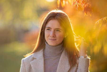 Portrait of pretty redhead girl in coat walking in forest at sunset in autumn