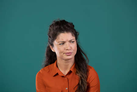 Portrait of young woman feeling unsure against green background.の写真素材