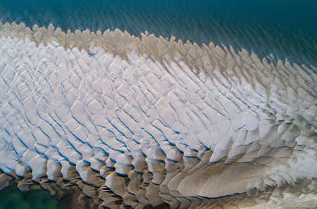 Aerial image of sandy dunes on river coast during low water level. Abstract image of beige earth texture against blue backgroundの写真素材
