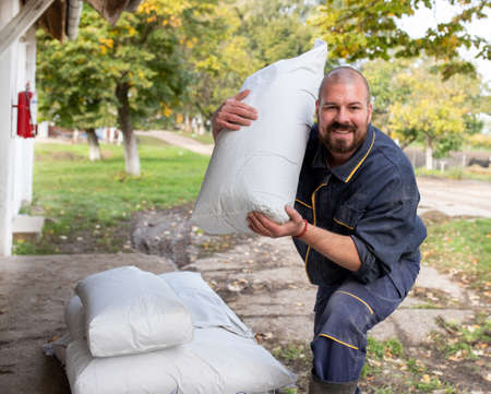 Happy farm worker holding bag of livestock food on a farm and looking at camera.の写真素材