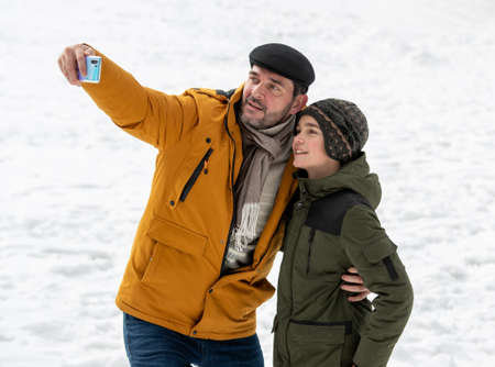 Father and son taking selfie on snow in park during winter holidaysの写真素材