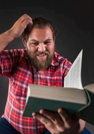 Young man feeling uncertain while reading a book.
