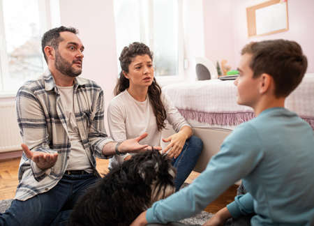 Angry parents having serious talk with boy in his room, sitting on floor