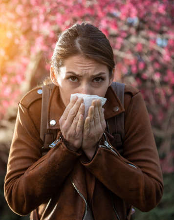 Young pretty girl blowing nose in front of blooming tree. Spring allergy reactionの写真素材
