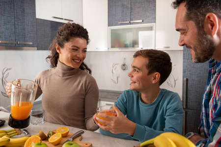 Family spends time together in the kitchen and drinks freshly squeezed orange juice.