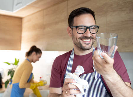 Portrait of a smiling man with apron holding a glass in his hand and polishing it with a cloth.の写真素材