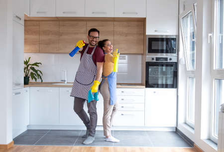 Young couple in the kitchen with cleaning supplies wearing gloves and doing their chores together.