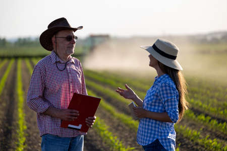 Two farmers young woman and senior man talking in soybean field in spring time at sunsetの写真素材