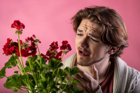 Young man with beard and make up feeling unhappy because of dry flowersの写真素材