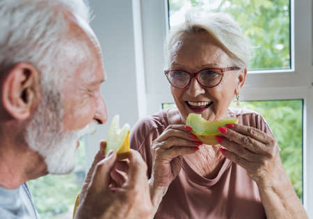 Senior couple sitting at dining table at home and eating melon in summer timeの写真素材