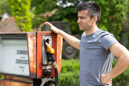 Disappointed man standing beside old rusty gasoline pump out of serviceの写真素材