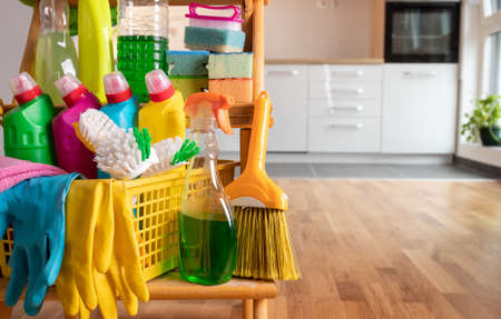 Close up of cleaning products arranged on wooden shelves in front of kitchen. Housekeeping concept