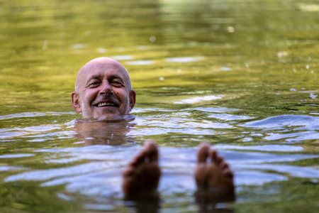Happy senior man swimming in green water river in summerの写真素材