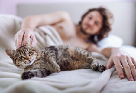 Young man cuddling cute tabby cat in bedの写真素材