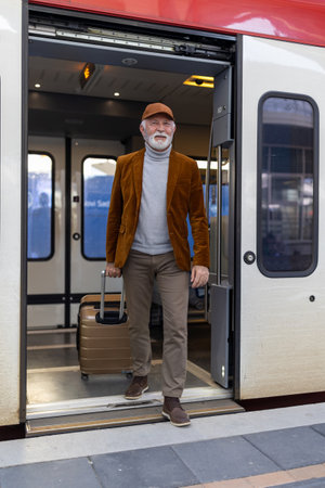 Senior man with suitcase getting out of train on terminal at stationの写真素材