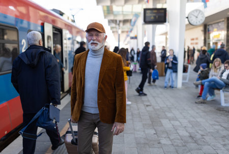 Senior man pulling suitcase in front of train on terminal at stationの写真素材