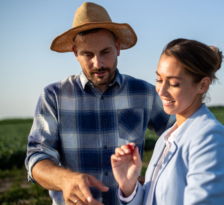 Pretty business woman and handsome farmer signing documents on field in summer time