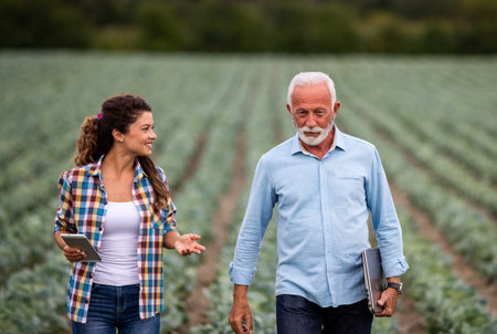 Senior businessman and young farmer woman talking in cabbage plantation in summer time. Agribusiness...