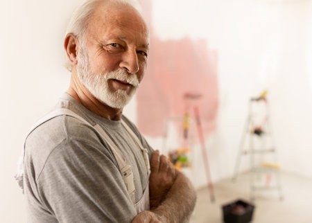 Portrait of senior man in white overalls painting room wall in pink color for granddaughterの写真素材